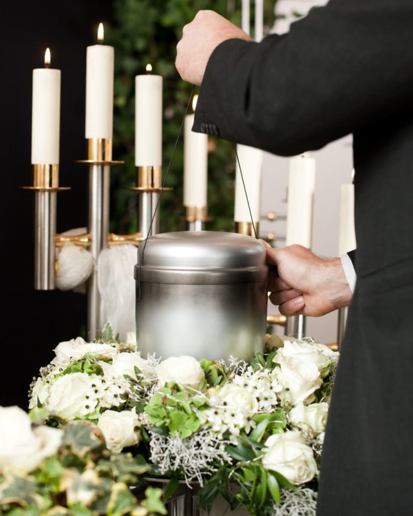 man-taking-funeral-urn-with-candles-flowers